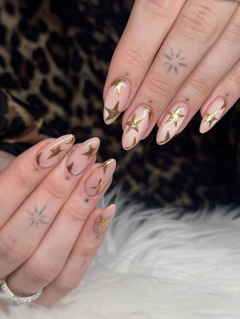 Gold chrome stars on almond nails, credited to Your Nail Crush